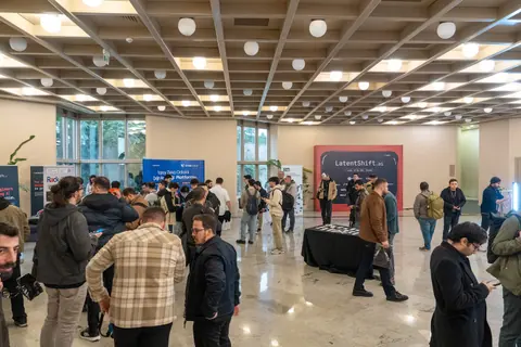 Attendees gather around booths and tables in the bright LatentShift foyer, with a large event backdrop against the far wall.