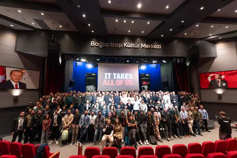 A large group poses in front of the LatentShift stage beneath a screen reading “IT TAKES ALL OF US.”