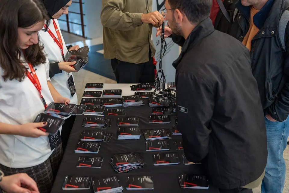 Two women sort black conference badges across a registration table as attendees gather on the other side.