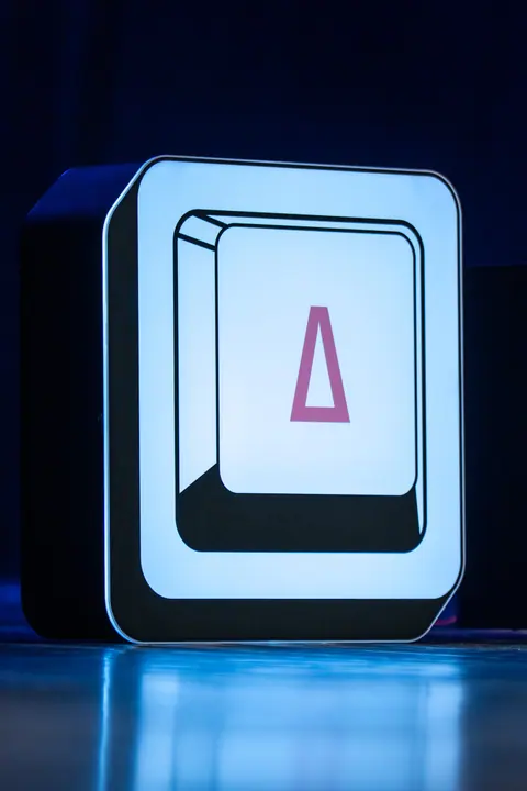 A close-up of the illuminated LatentShift logo, with a pink central symbol and blue light reflected on the stage floor.