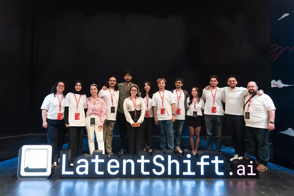 A group wearing conference badges poses behind the large illuminated LatentShift.ai sign, with several people resting arms around one another.