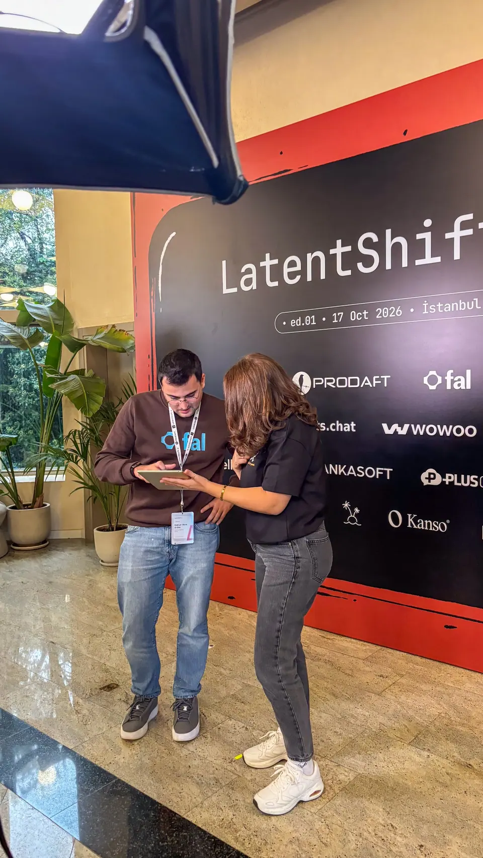 A man in a brown sweatshirt and a woman in a black shirt look down at a tablet beside the LatentShift backdrop.