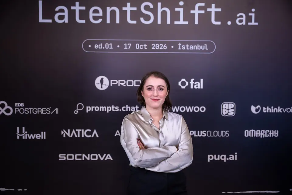 A woman in a silver blouse smiles at the camera with her arms folded in front of the LatentShift backdrop.
